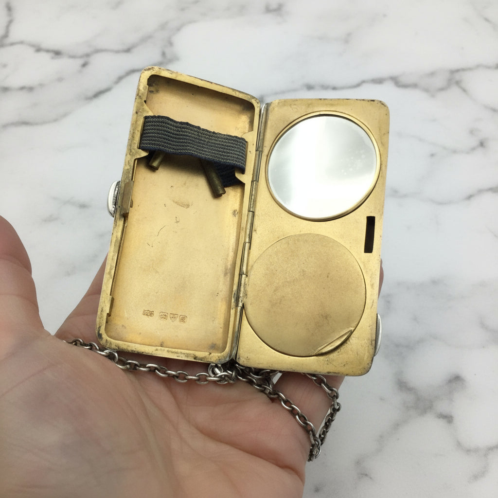 gilded golden inside of case showing a mirror, powder area and chain held in a hand with a marble background