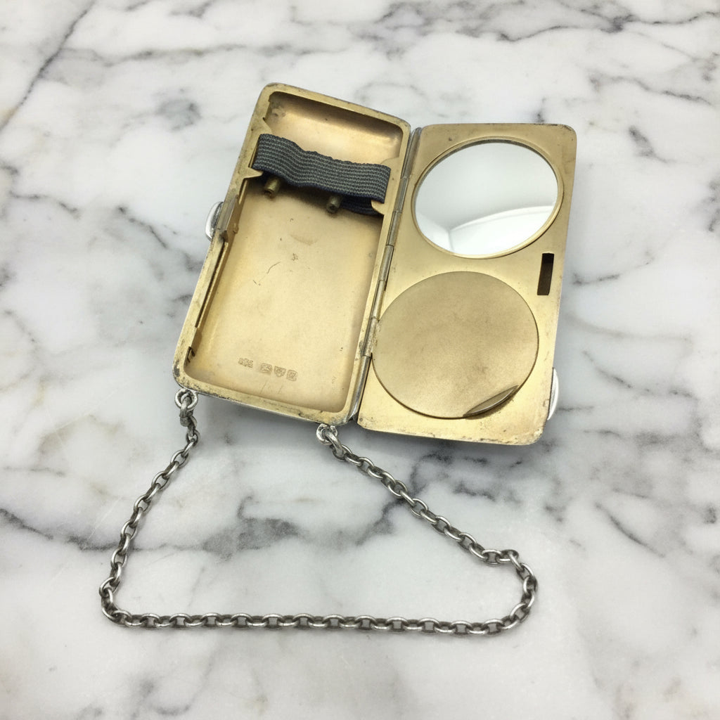 gilded golden inside of case showing a mirror, powder area and chain on a marble surface