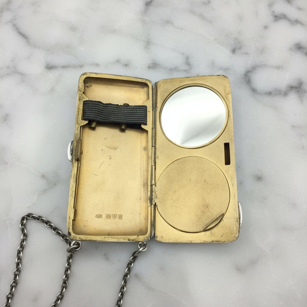 gilded golden inside of case showing a mirror, powder area and chain on a marble surface