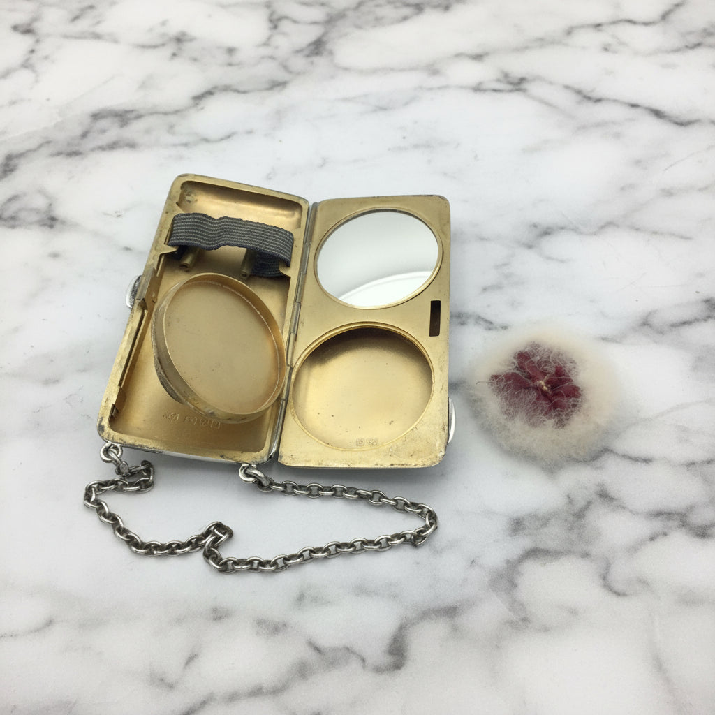gilded golden inside of case showing a mirror, powder area and chain, with the powder puff at the side on a marble surface