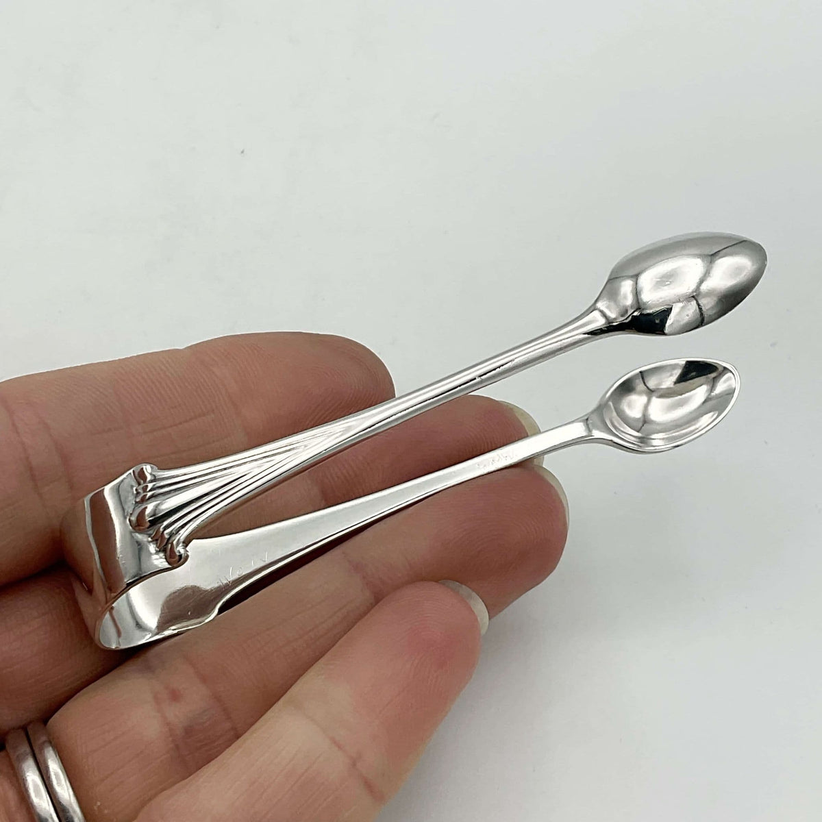 Silver sugar tongs showing an art deco design sitting on fingers