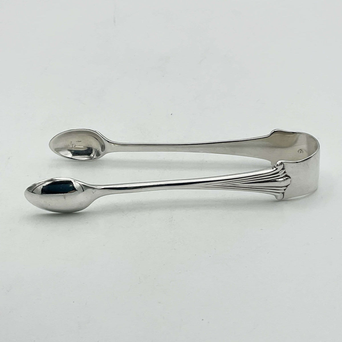 Silver sugar tongs showing an art deco design on a white background