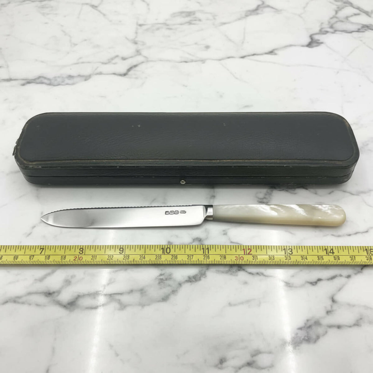 Knife with a black presentation box on a marble surface, measured by a tape measure.