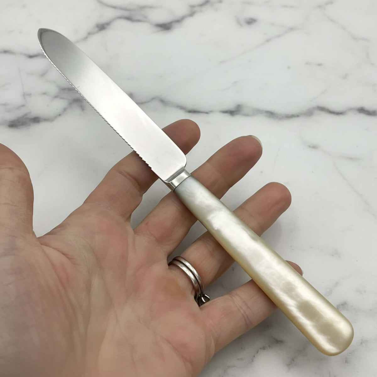 Hand holding a knife with a decorative handle on a marble surface