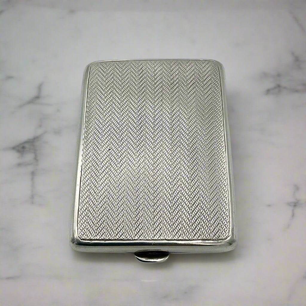 Antique sterling silver match case with a geometric pattern and a clasp on the front, displayed against a marble background 