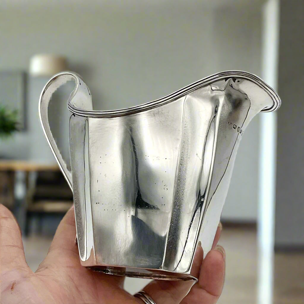 Antique silver jug held in a hand with a dining room background
