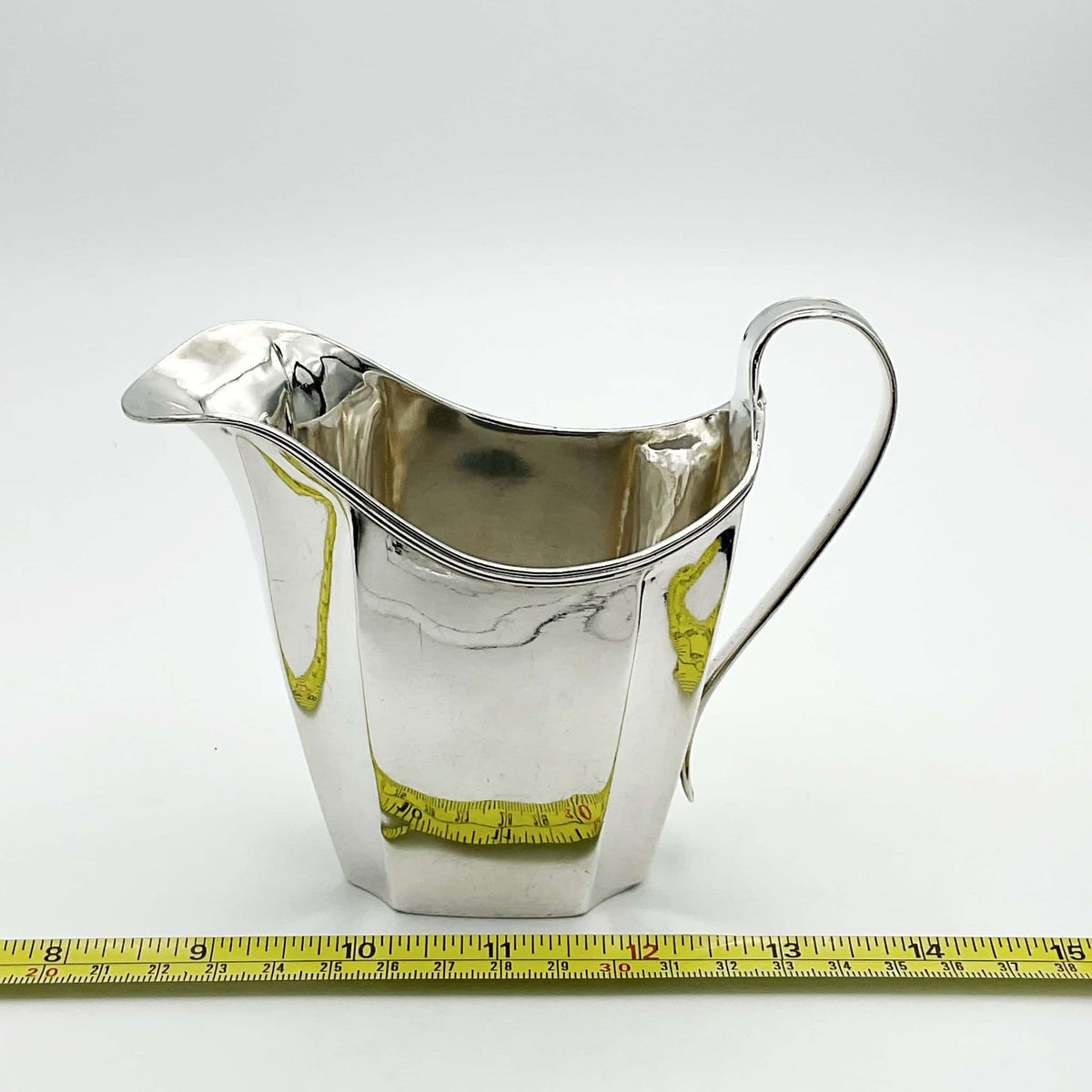 Antique silver jug next to a tape measure on a white background 
