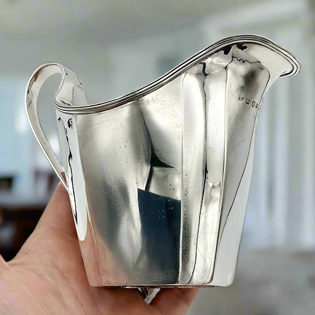 Silver jug held in a hand with a dining room in the background