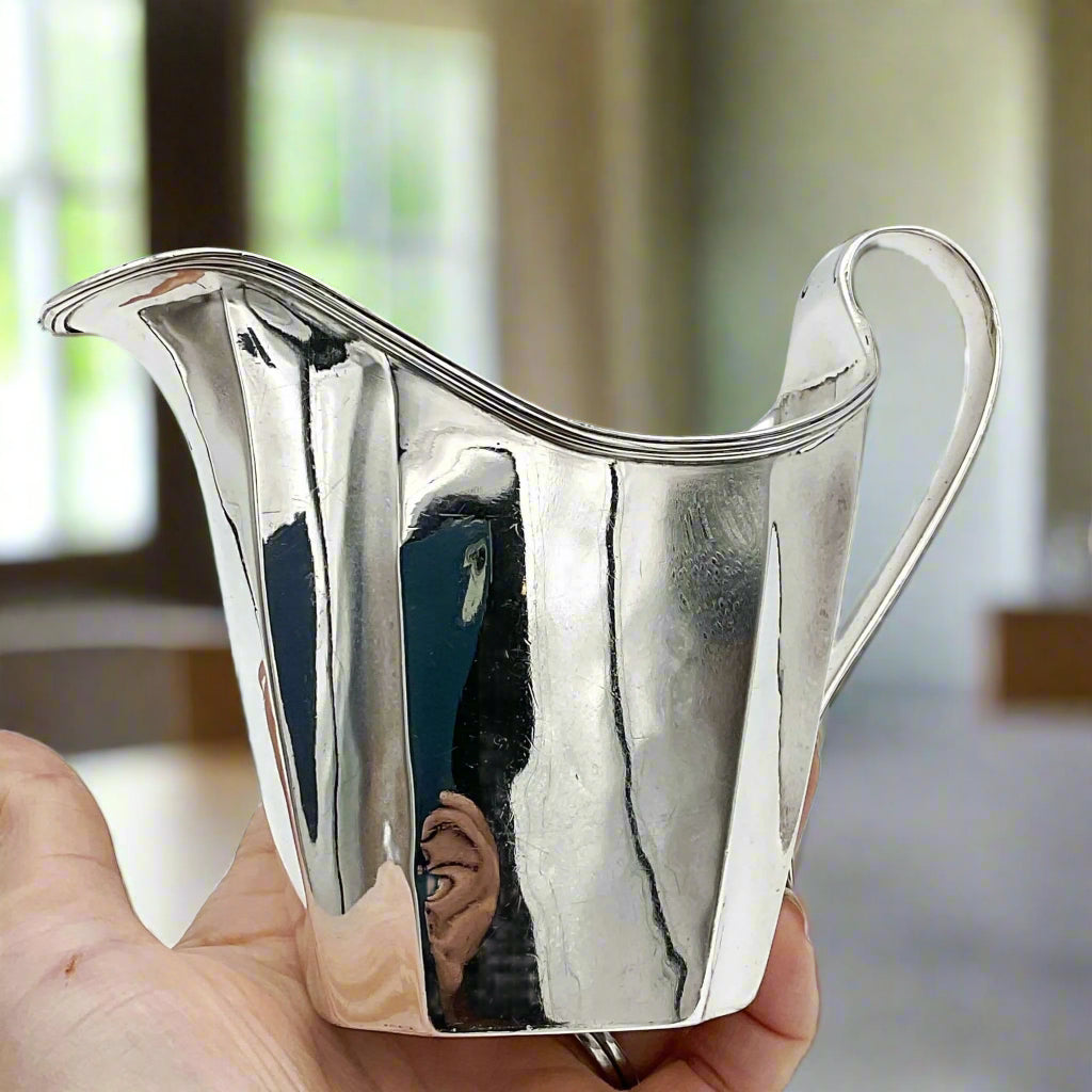 Silver jug half in a hand with a dining room background 
