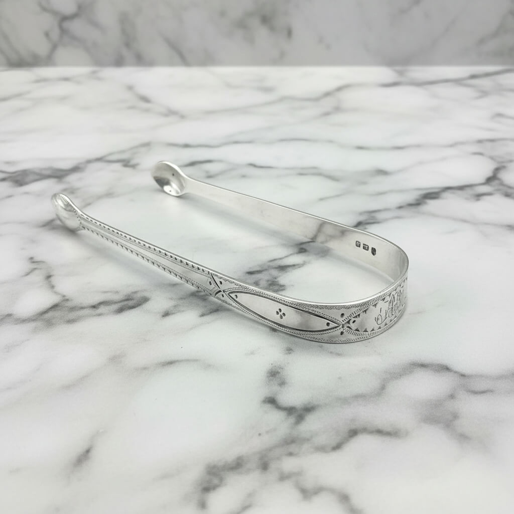 Antique silver sugar tongs on a marble surface