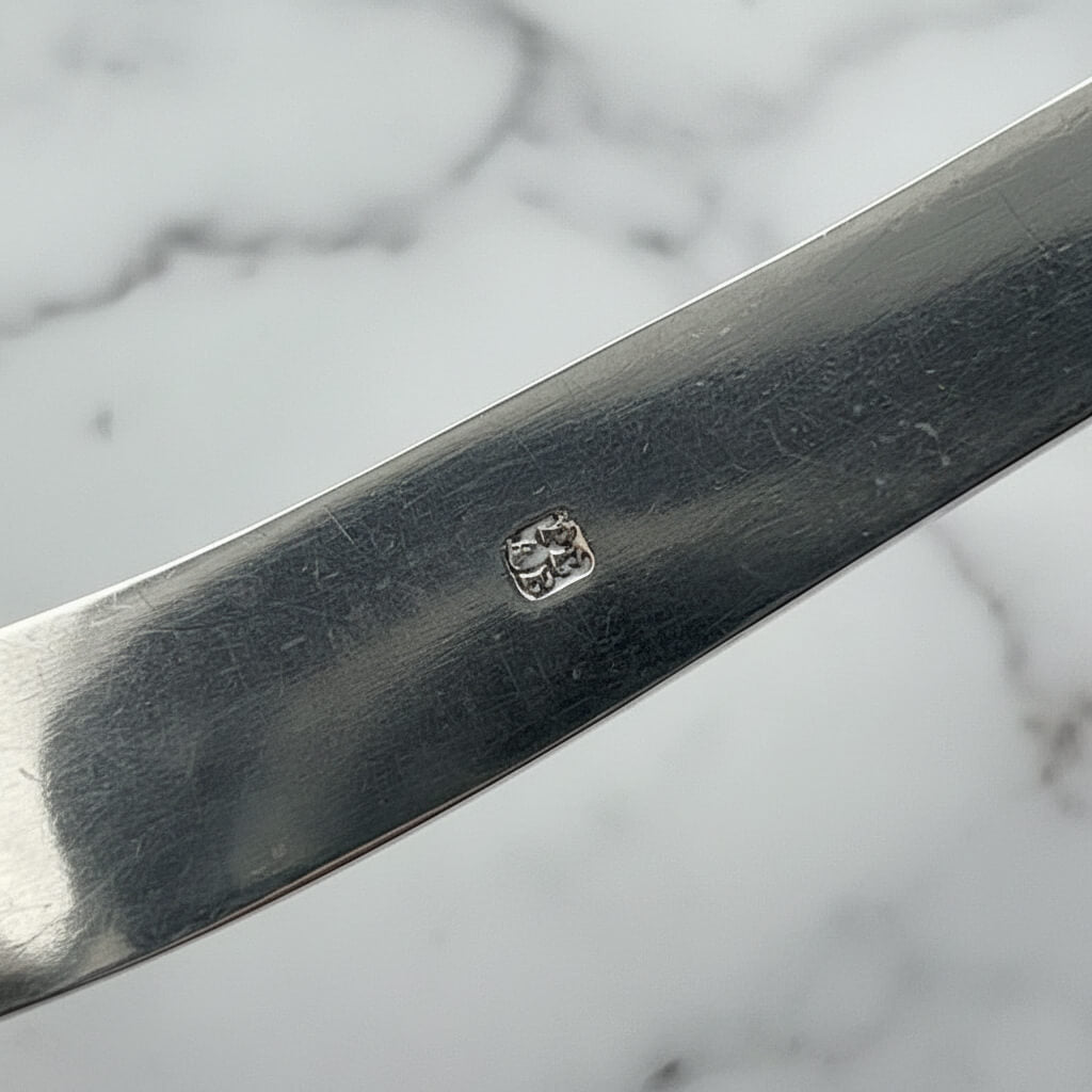 makers marks on side of silver sugar tongs with a marble background