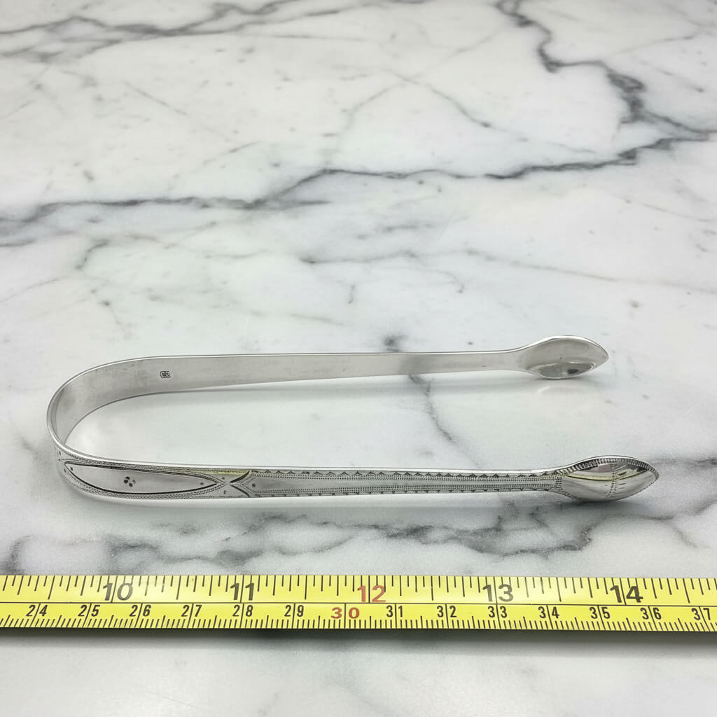 silver sugar tongs next to a tape measure for scale on a marble worktop
