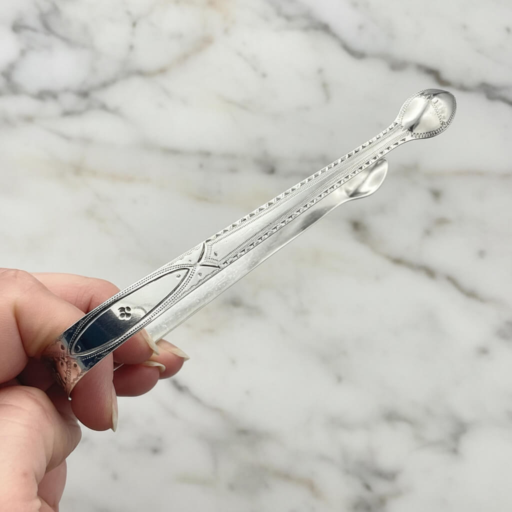 side of antique sugar tongs held in a hand with a marble worktop in the background