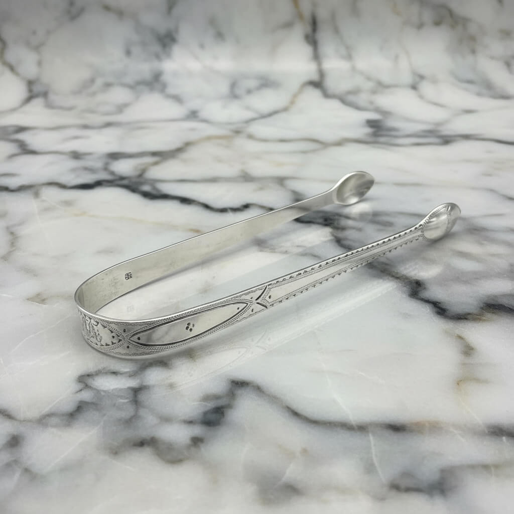 Antique silver sugar tongs on a marble surface