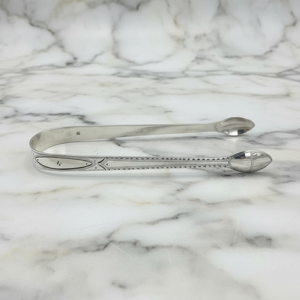 side view of antique silver sugar tongs on a marble surface