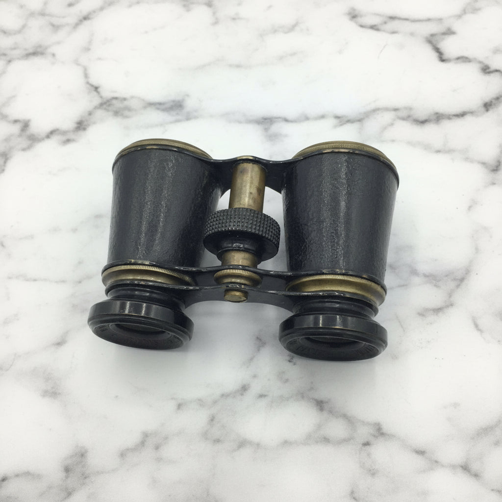 Antique binoculars with black and brass finish on a marble background