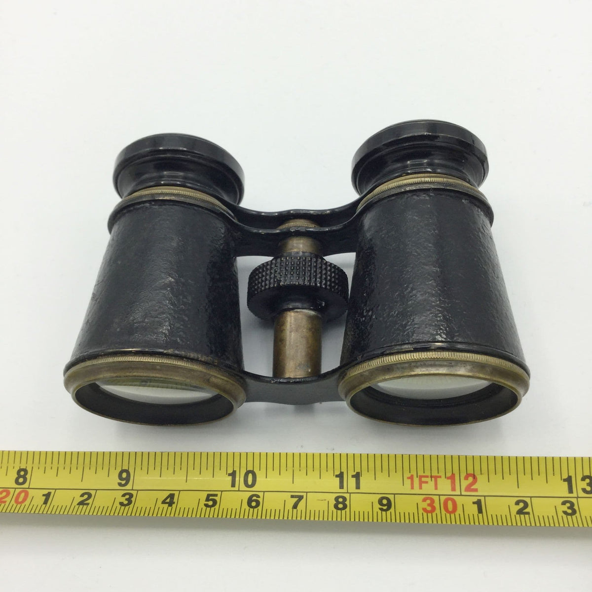 antique black binoculars on a marble surface next to a tape measure for scale