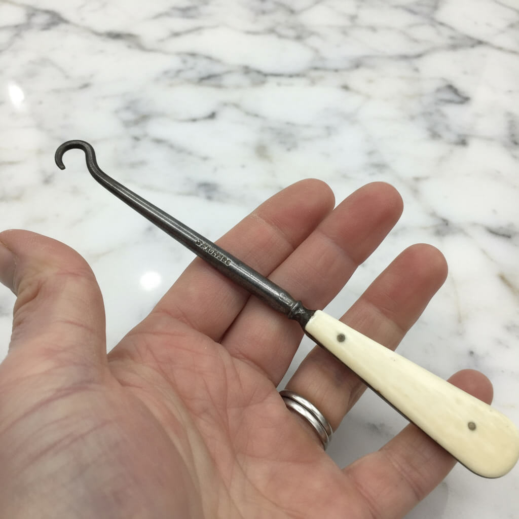 Antique bone handled button hook held in a hand