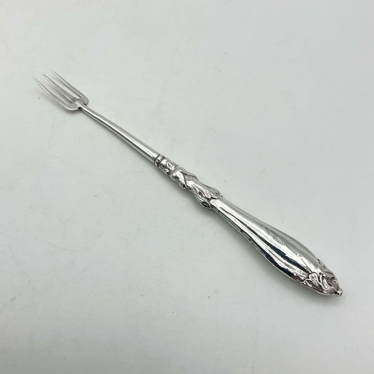 Antique silver plated pickle fork with an ornate handle on a plain background 