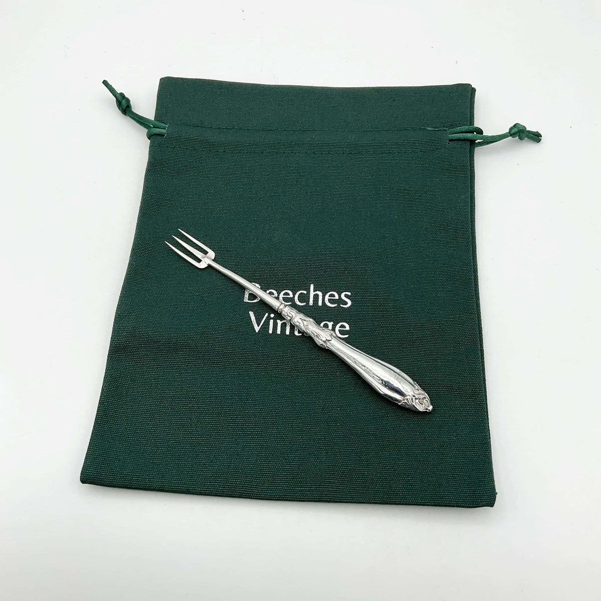 Antique silver plated pickle fork with an ornate handle on a green cotton gift bag