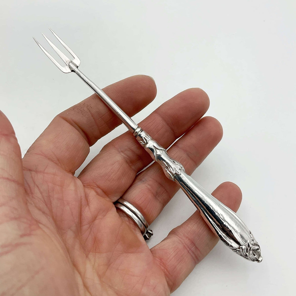 Antique silver plated pickle fork with an ornate handle held in a hand