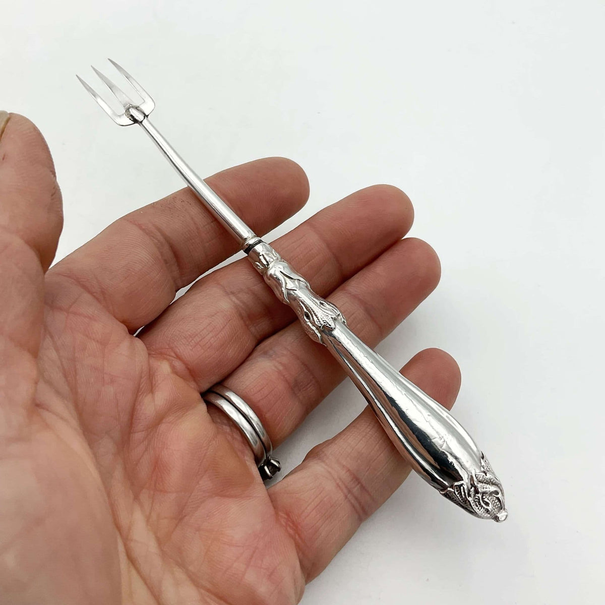 Antique silver plated pickle fork with an ornate handle held in a hand