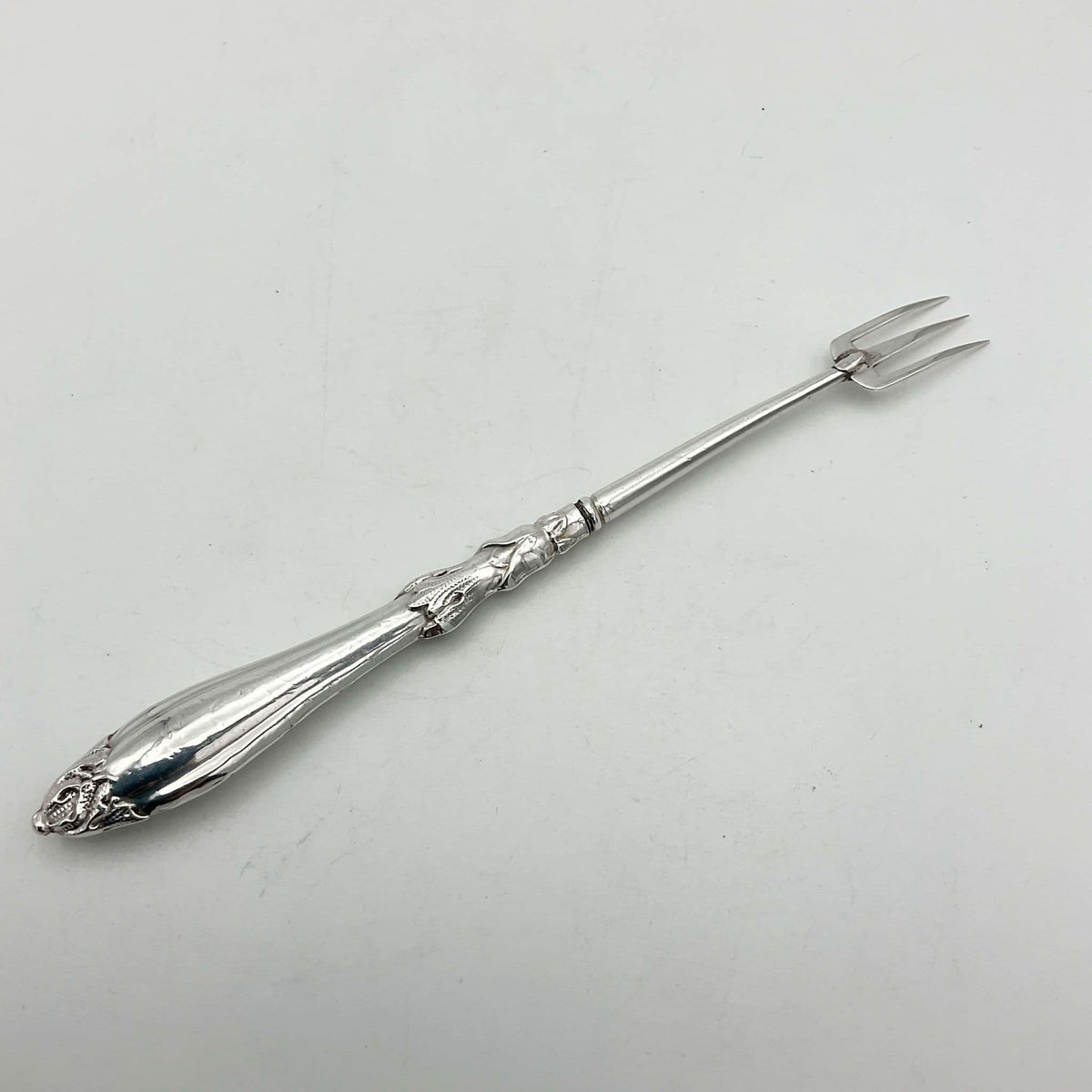 Back view of Antique silver plated pickle fork with an ornate handle on a plain background 