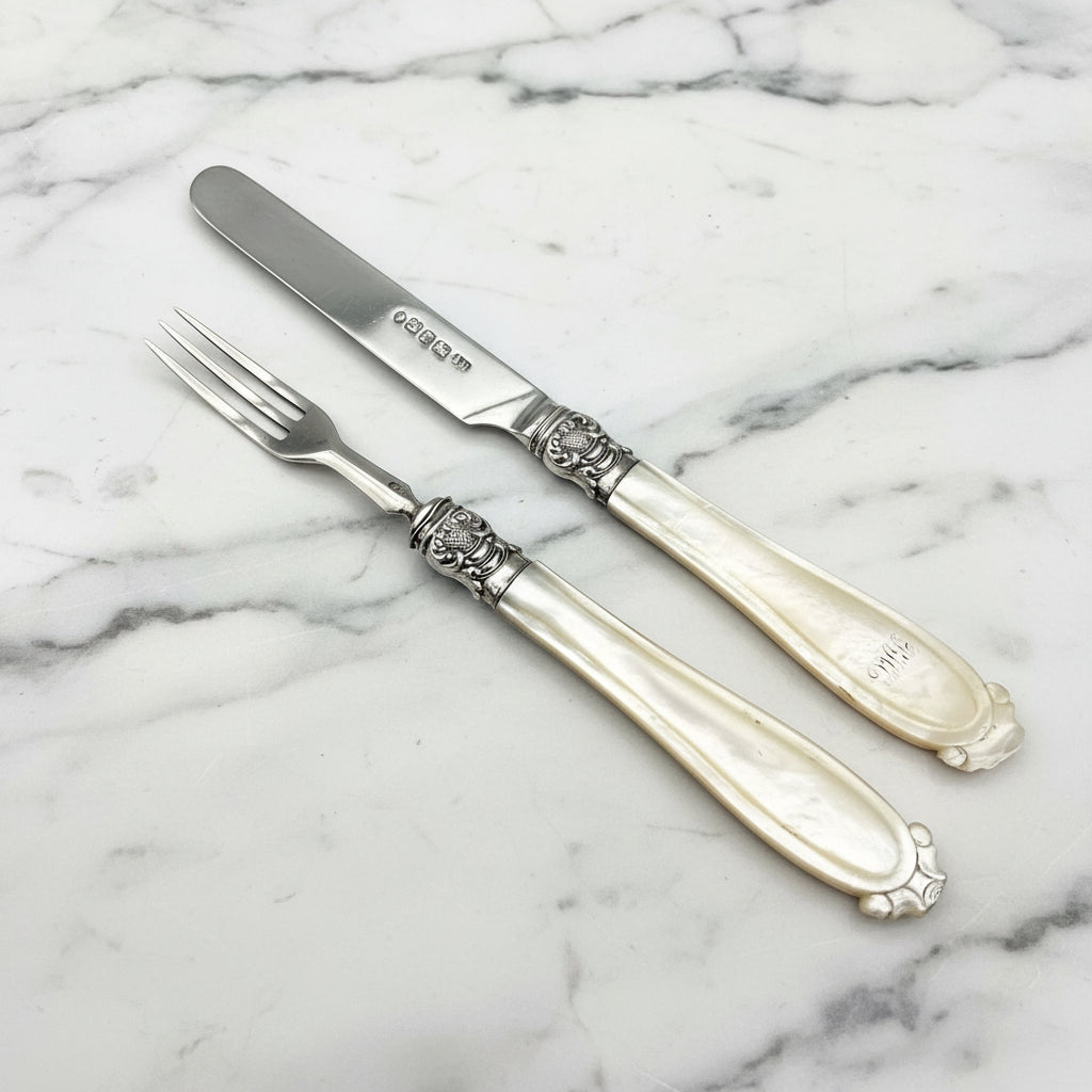 Antique silver knife and fork set with ornate collars and mother of pearl handles.