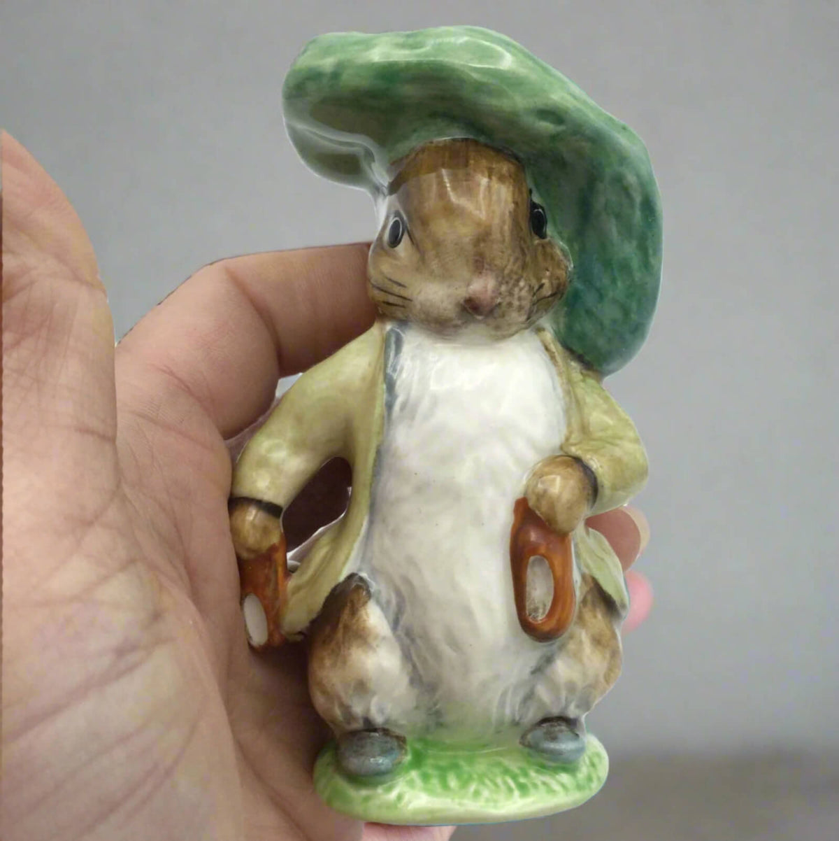 Hand holding a ceramic rabbit figurine with a green hat against a plain background