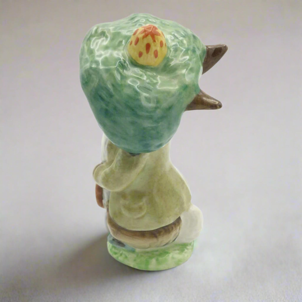 Ceramic figure of a character with a green hat and body on a plain background