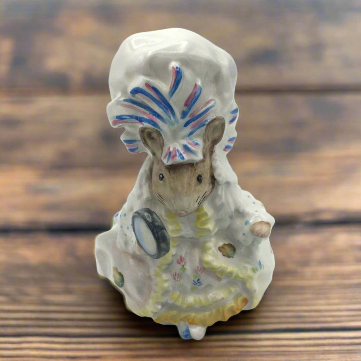 Small ceramic figure of a mouse with a colorful hat on a wooden surface