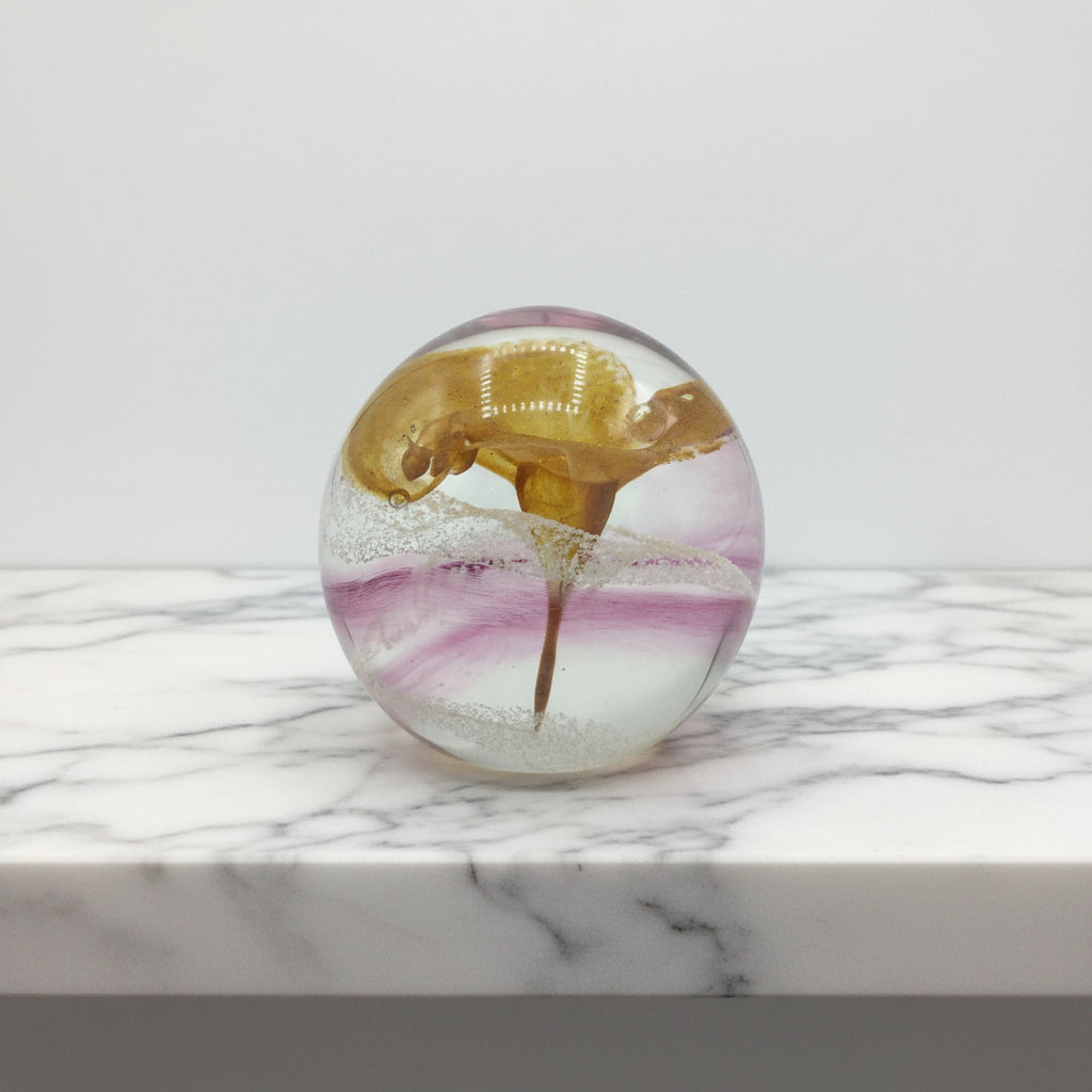 Glass paperweight with a gold and pink design on a marble surface