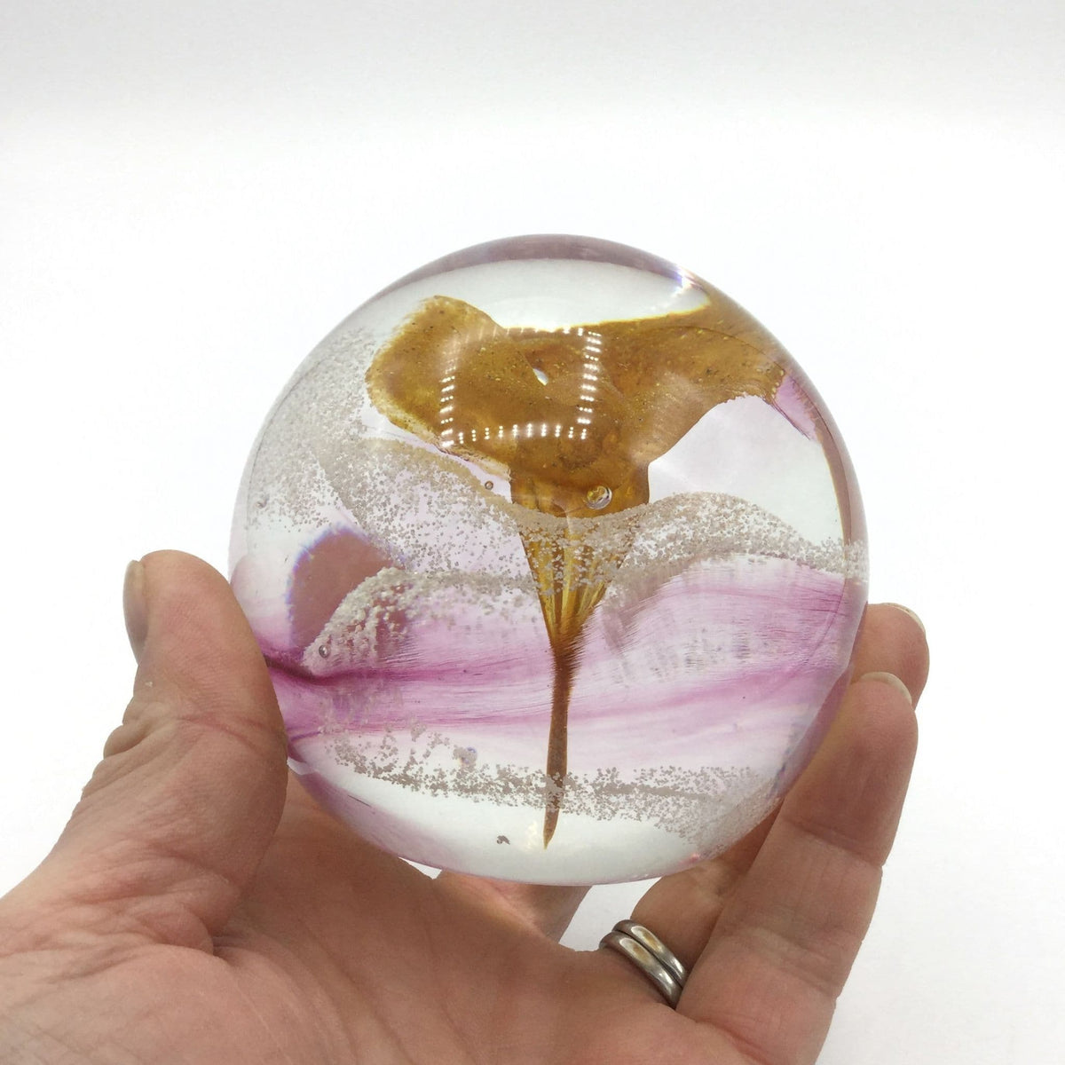 caithness paperweight held in a hand featuring an orange flower and pink swirls inside