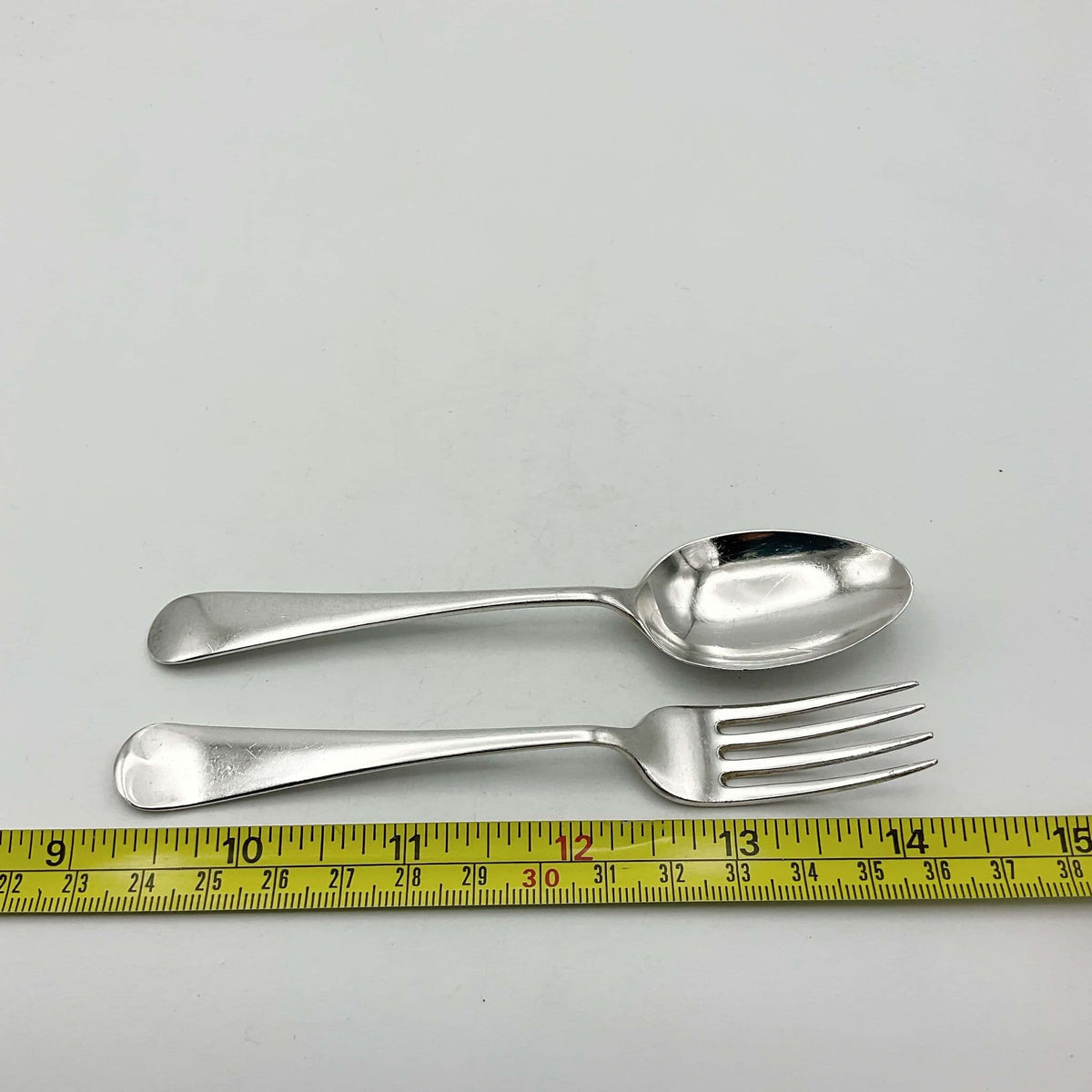 Silver spoon and fork next to tape measure showing they measure approximately 13cm in length