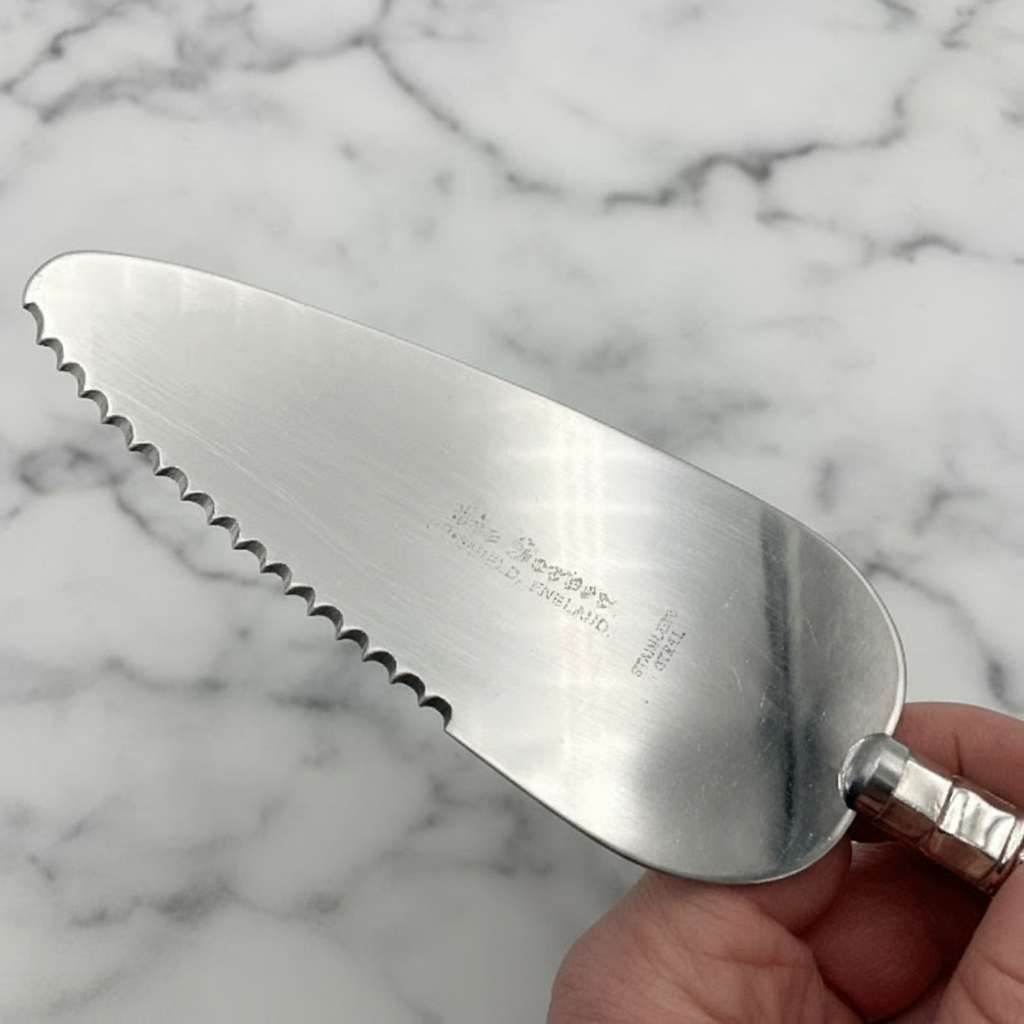 Steel cake server with a serrated edge held by a hand against a light marble background