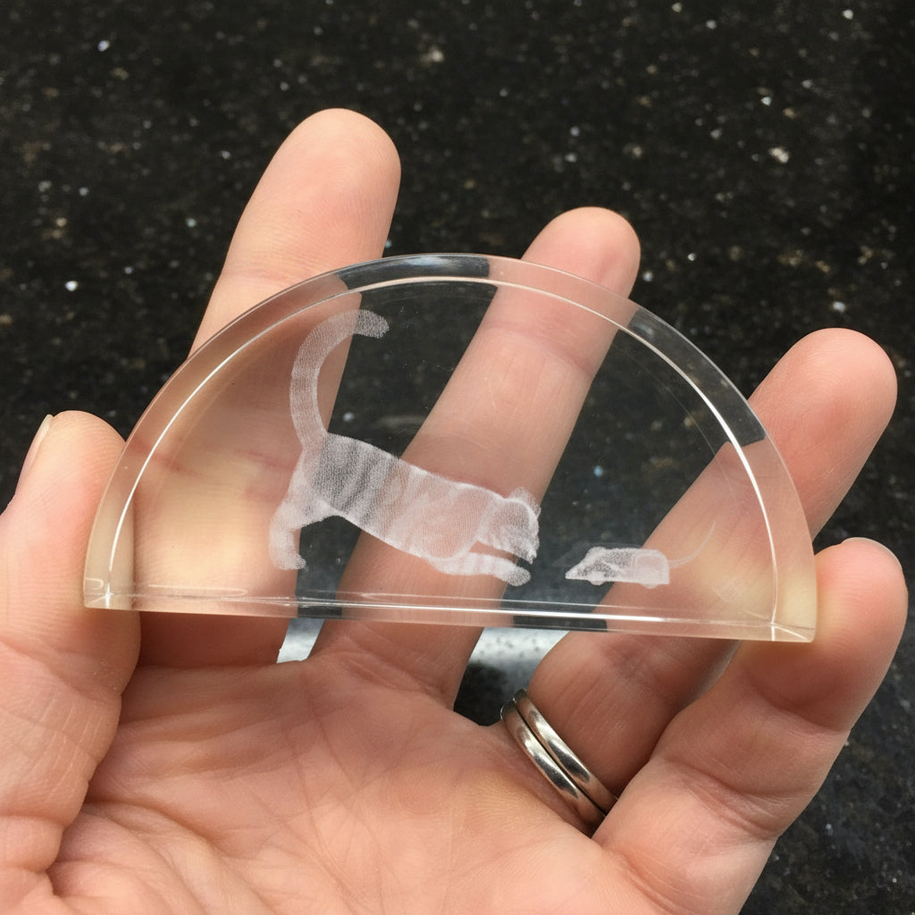 crystal paperweight half-moon shaped object with a cat and mouse design held in a hand against a black background