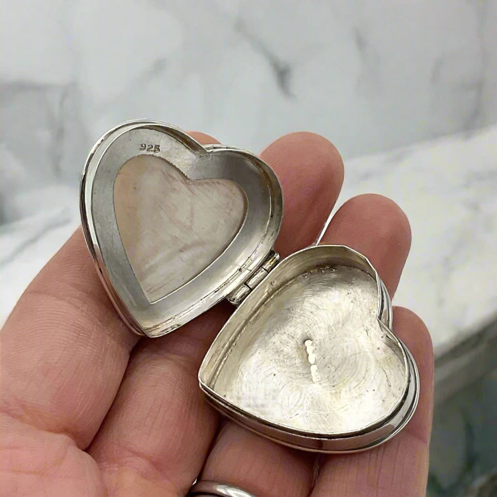 Inside of Heart shaped silver pill box in a hand on a marble worktop background.