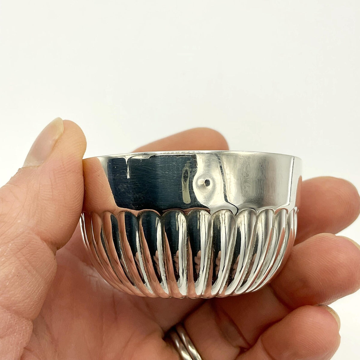 Silver bowl held in a hand against a white background