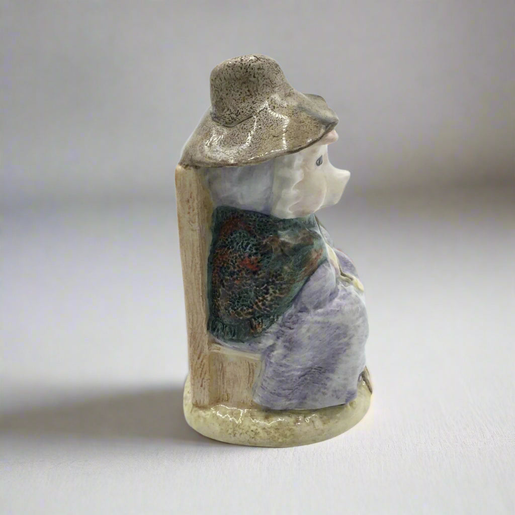 Small ceramic figurine of a pig wearing a hat and scarf on a plain background