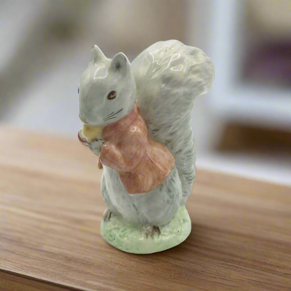 Squirrel figurine holding a acorn on a wooden surface with a gray background
