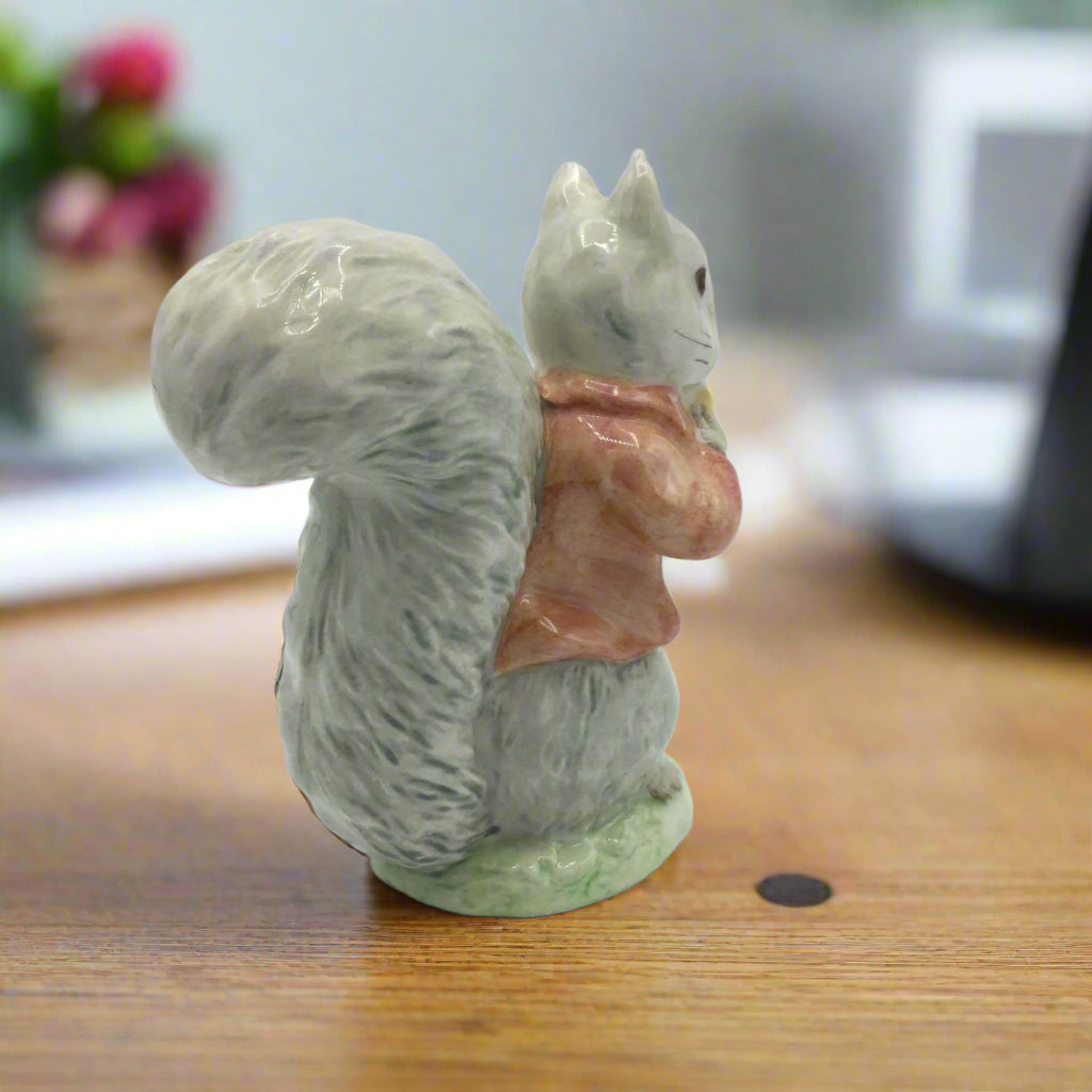 Squirrel figurine with a pink jacket on a wooden surface
