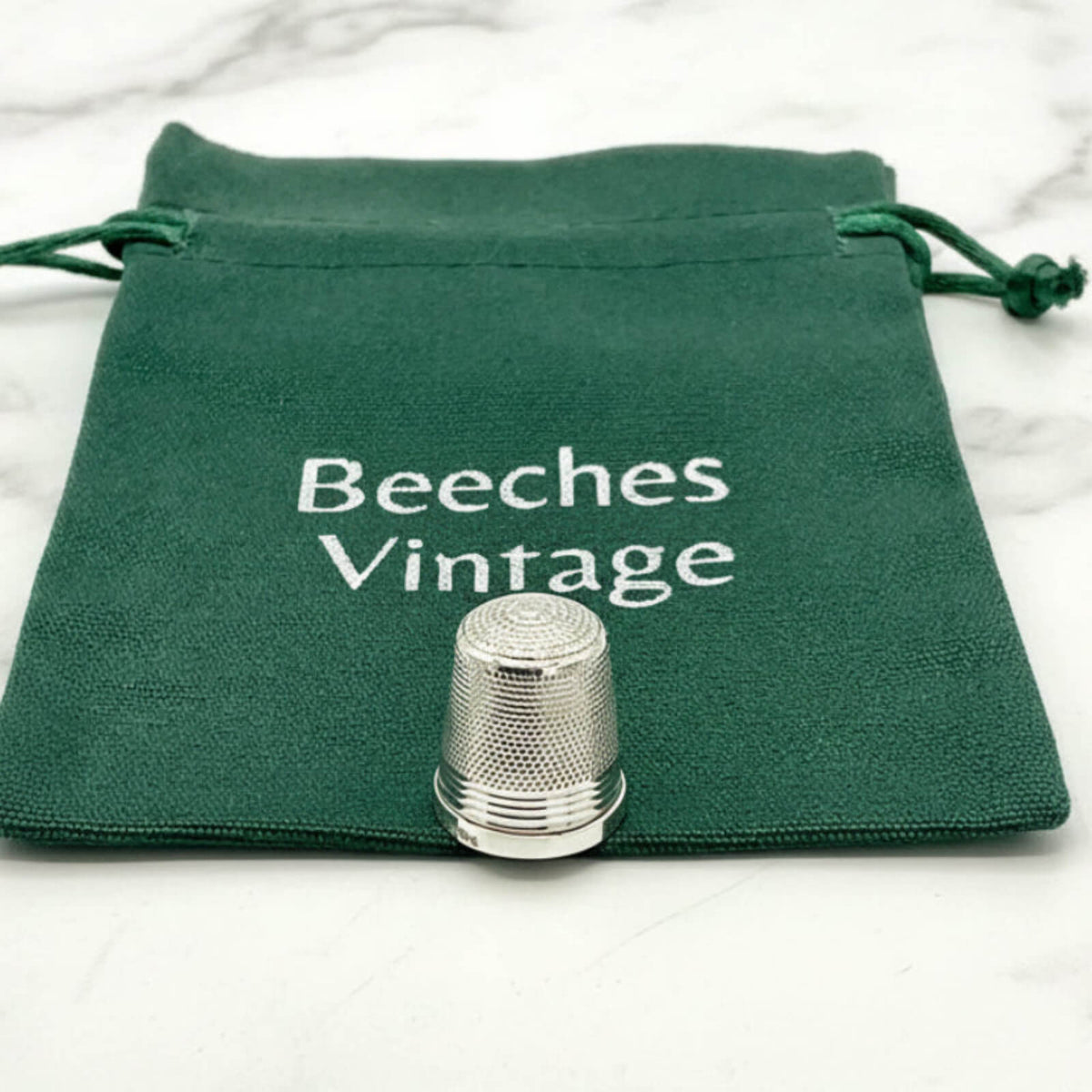 Silver thimble on a green drawstring bag with 'Beeches Vintage' text.