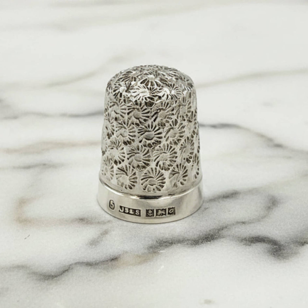 Silver thimble with intricate floral patterns on a marble surface