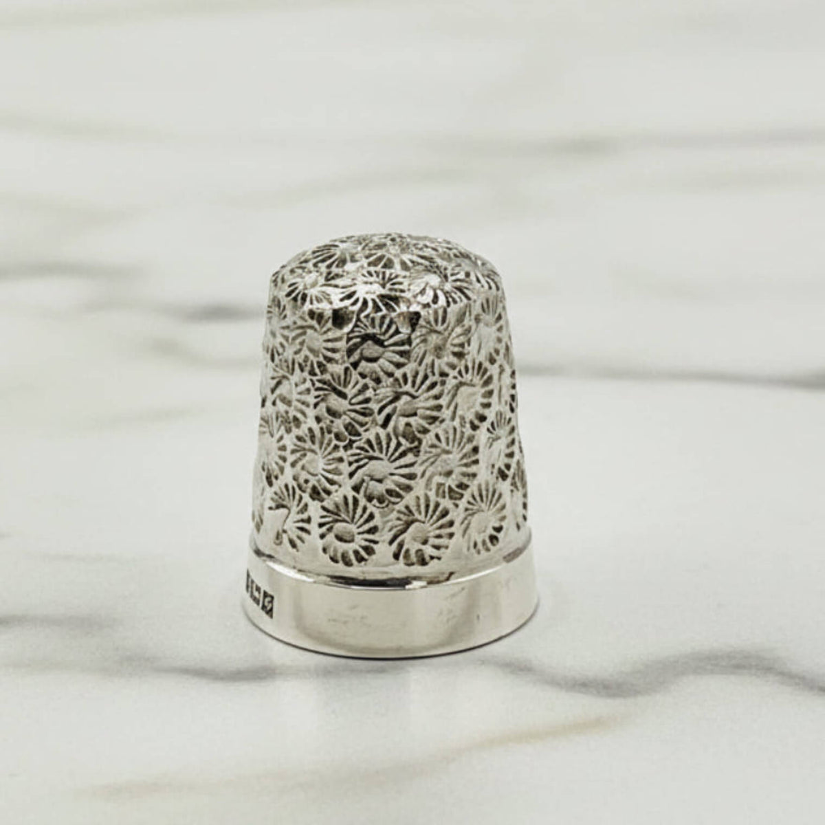 Silver thimble with intricate floral pattern on a marble surface