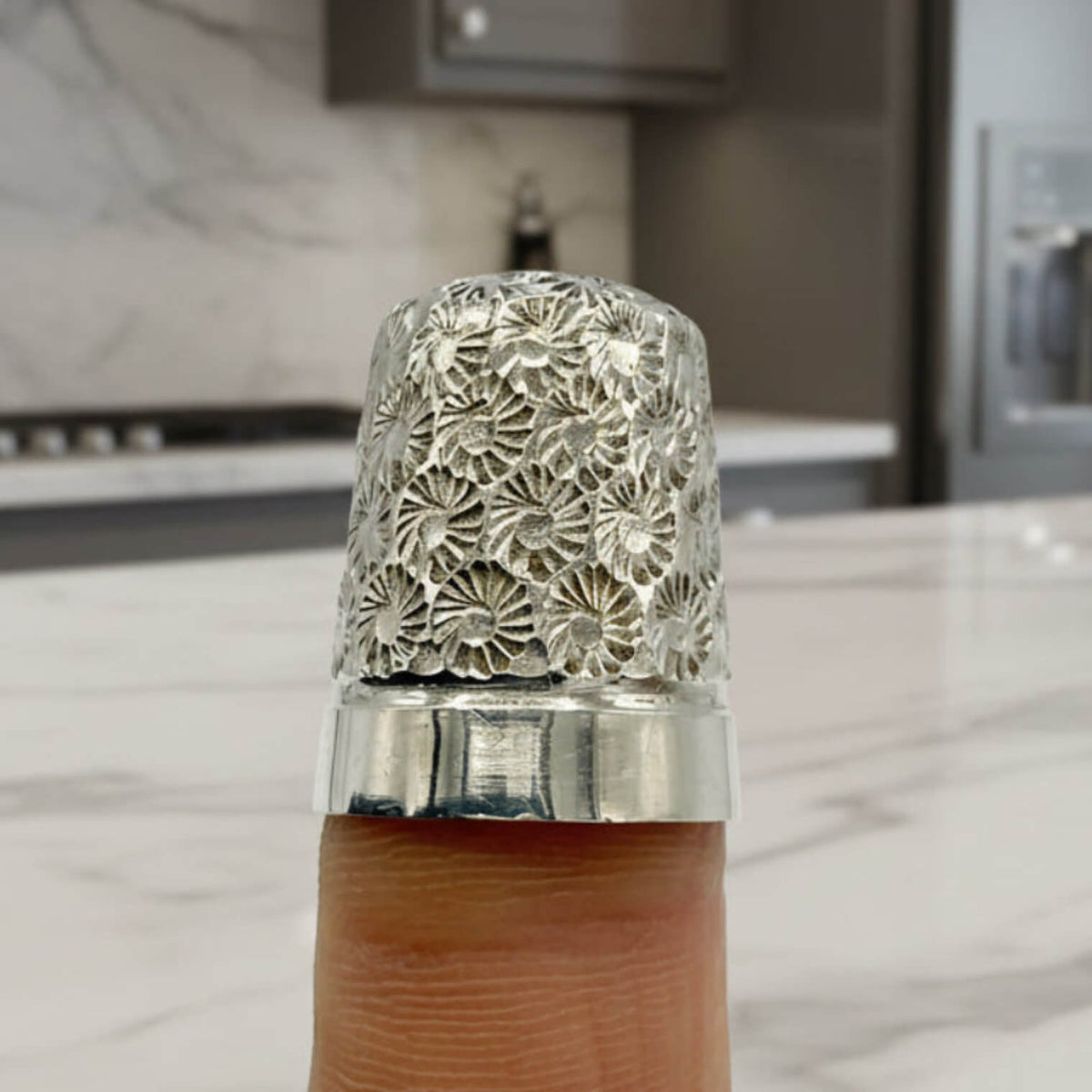 Decorative silver thimble on a finger with a blurred kitchen background