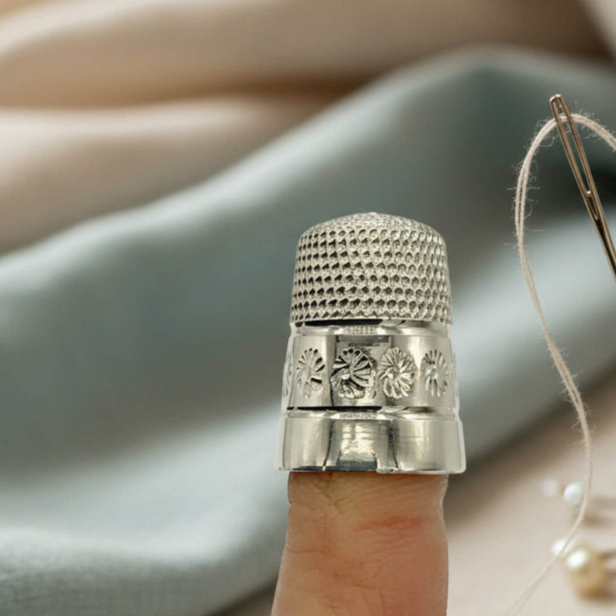Silver thimble on a finger with a blurred fabric background