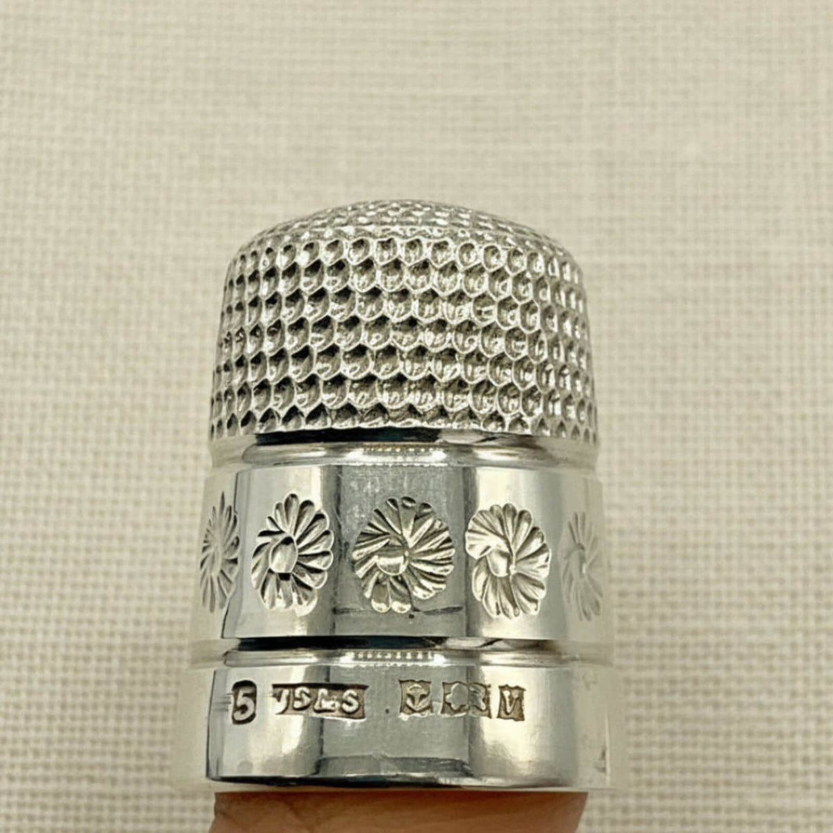 Silver thimble with floral patterns on a beige fabric background