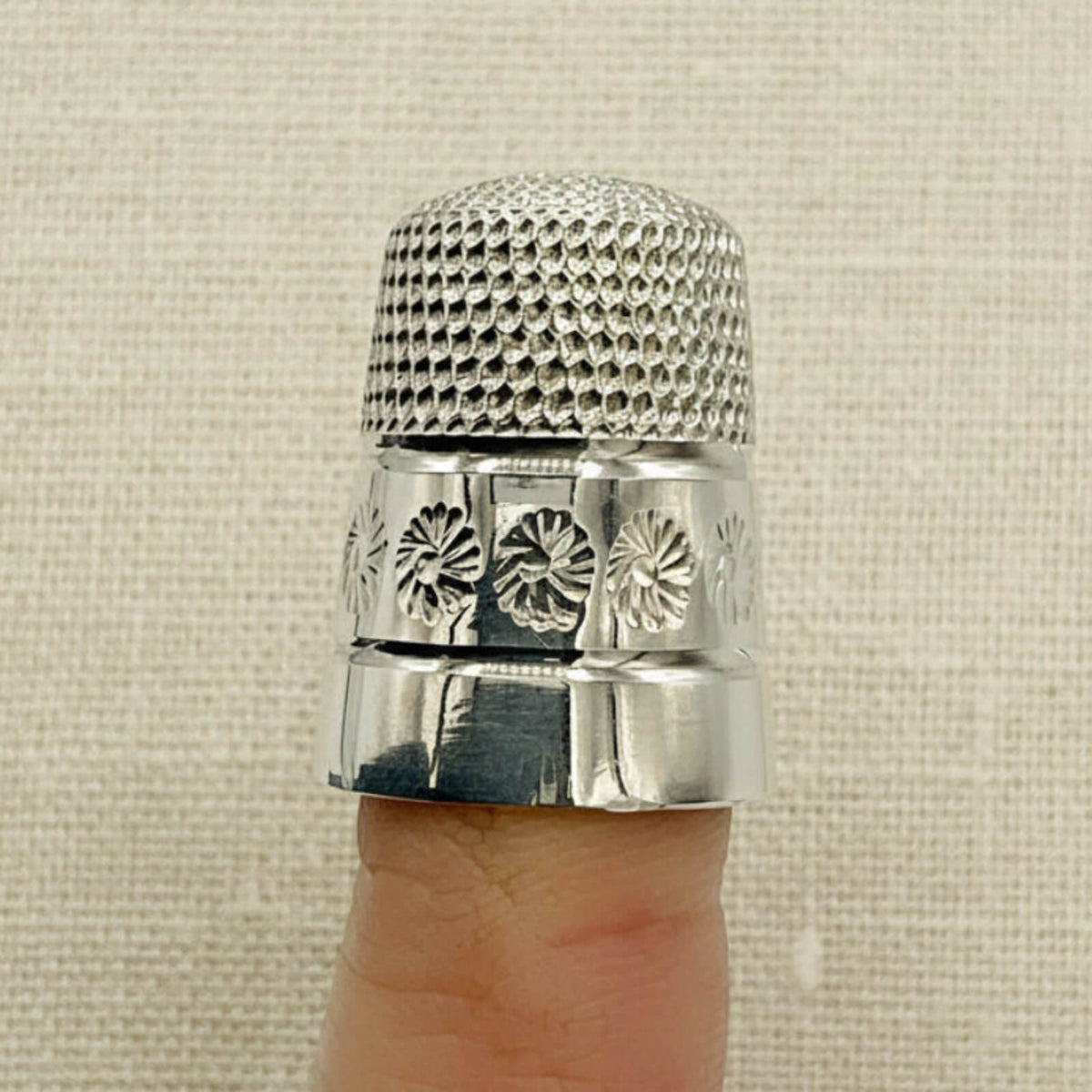 silver thimble on a finger with a beige material background