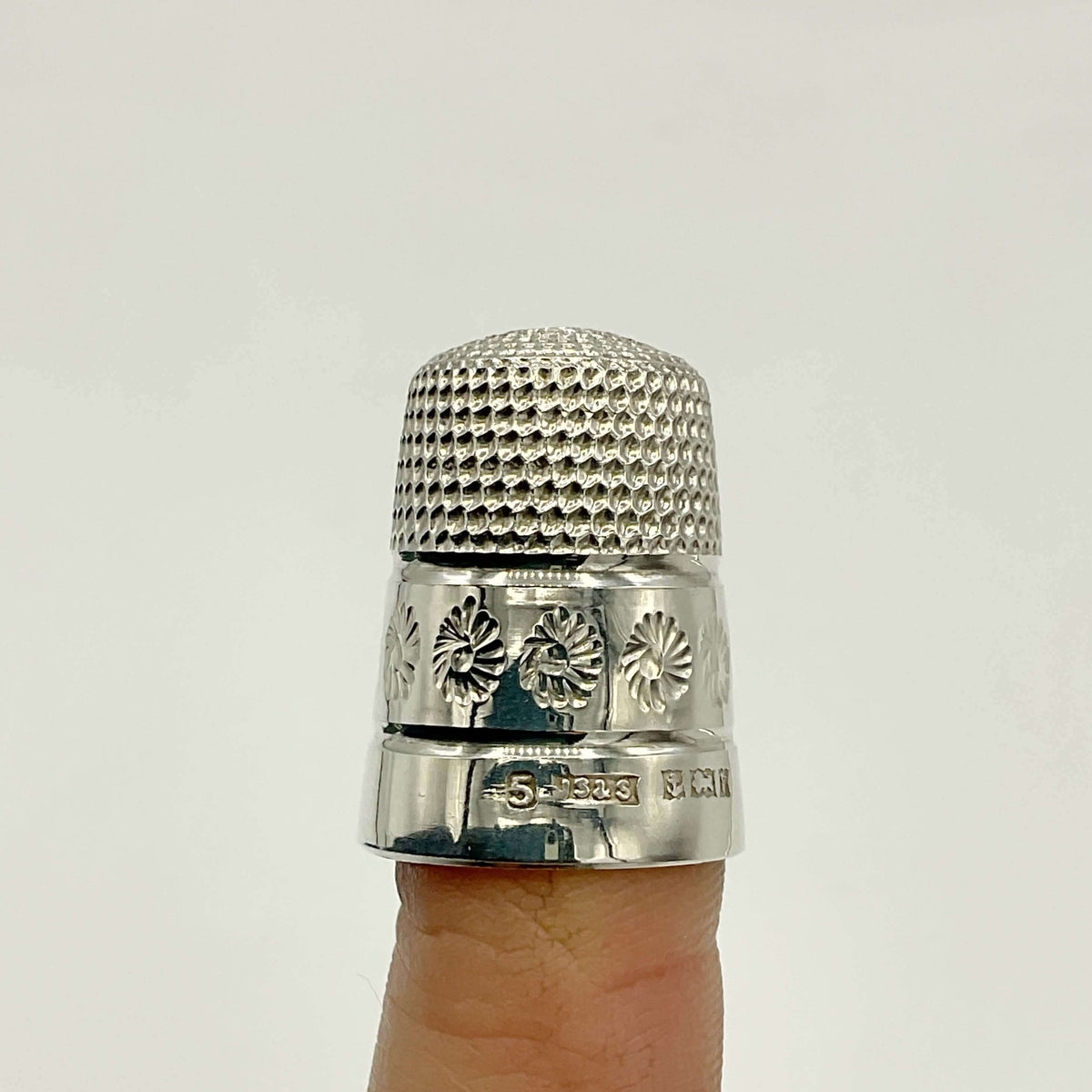 Silver thimble on a finger against a light gray background