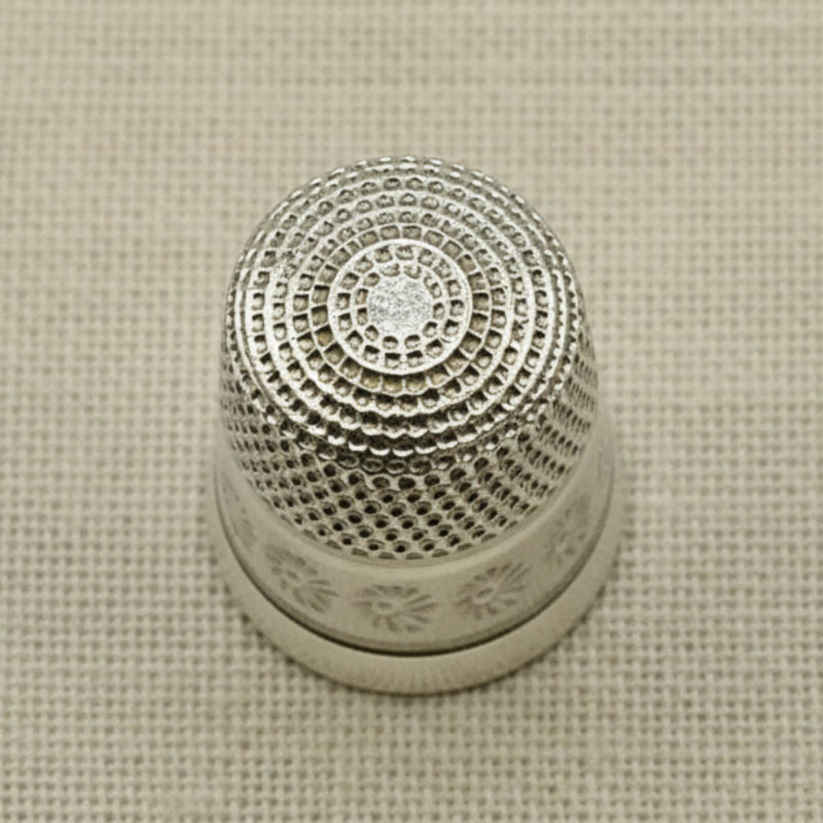 Silver thimble with intricate design on a beige fabric background